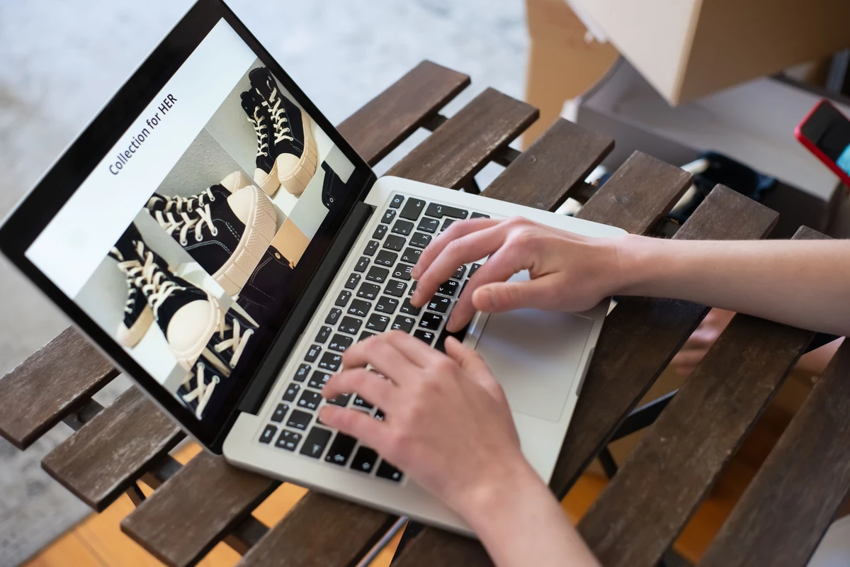 Jak przygotować strategię content SEO dla sklepu internetowego krok po kroku Dłonie przy laptopie ze stroną kolekcji w internetowym sklepie z obuwiem