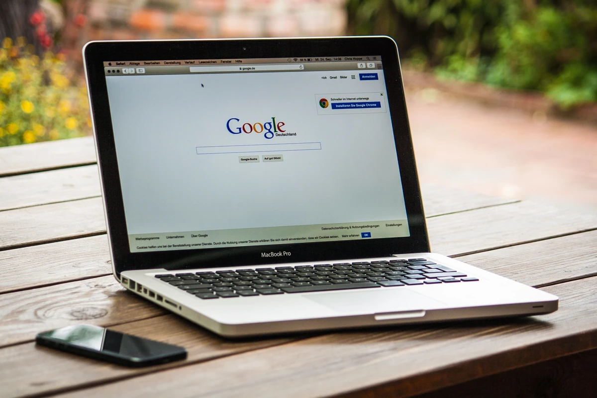 Czynniki rankingowe Google: co realnie wpływa na pozycje w SEO? Laptop z wyszukiwarką Google na drewnianym stole na zewnątrz, obok smartfon