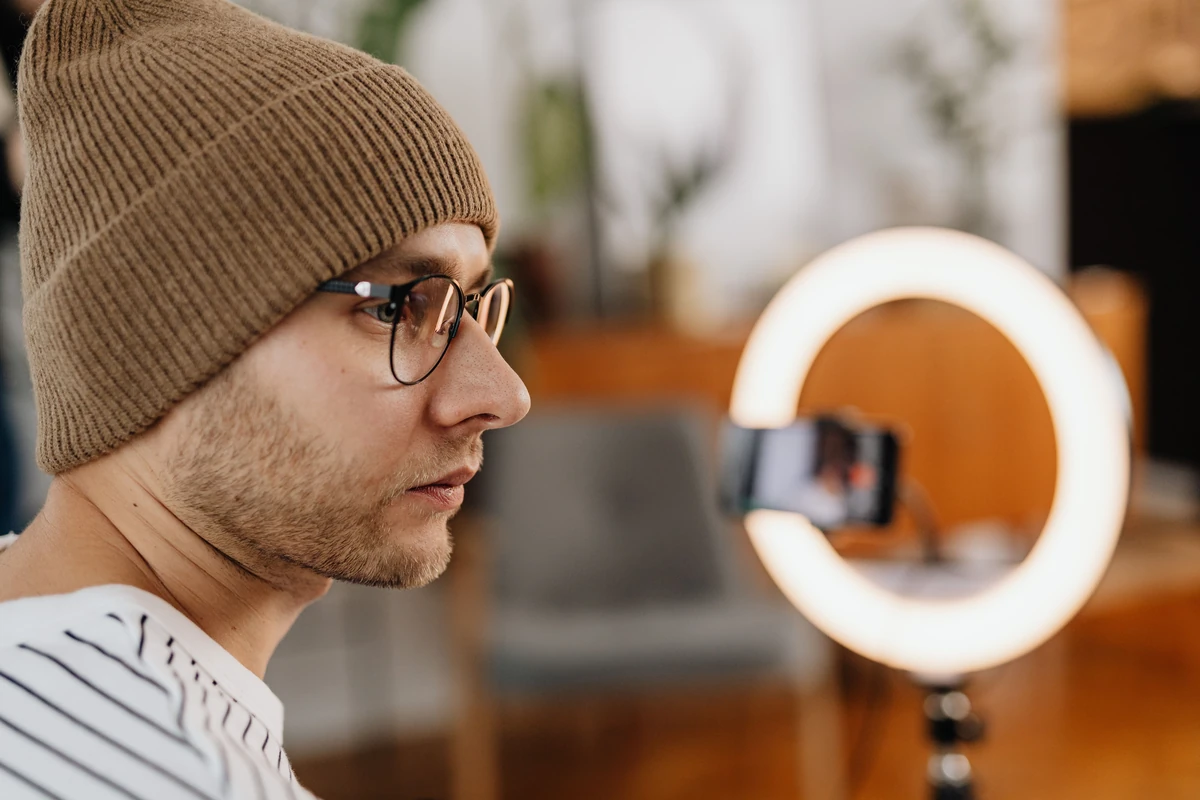 Influencerzy i social media a widoczność w Google: co naprawdę działa? Mężczyzna w okularach i czapce nagrywa wideo w domu smartfonem z lampą pierścieniową