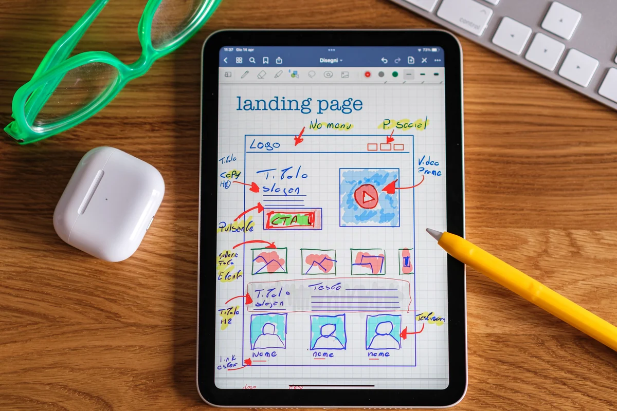 Landing page dla kampanii: jak projektować strony, które nie marnują kliknięć Tablet z odręcznym szkicem makiety landing page, obok okulary, słuchawki i rysik