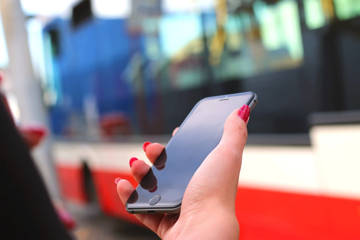 Pozycjonowanie strony one page: kiedy ma sens i jak zrobić to dobrze? Dłoń kobiety trzymającej smartfon na przystanku autobusowym
