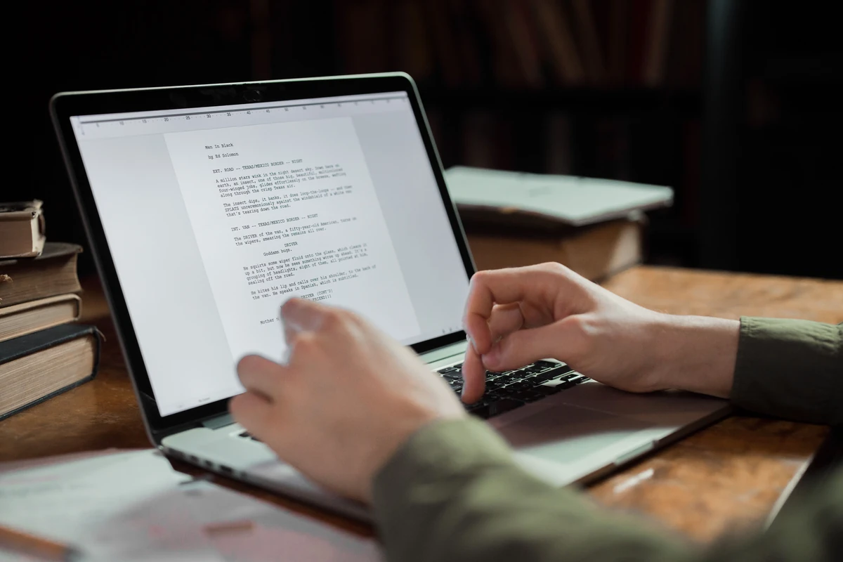 Optymalizacja treści: jak pisać teksty, które pomagają użytkownikowi i stronie Osoba pisze na laptopie w przytulnym miejscu pracy otoczonym książkami