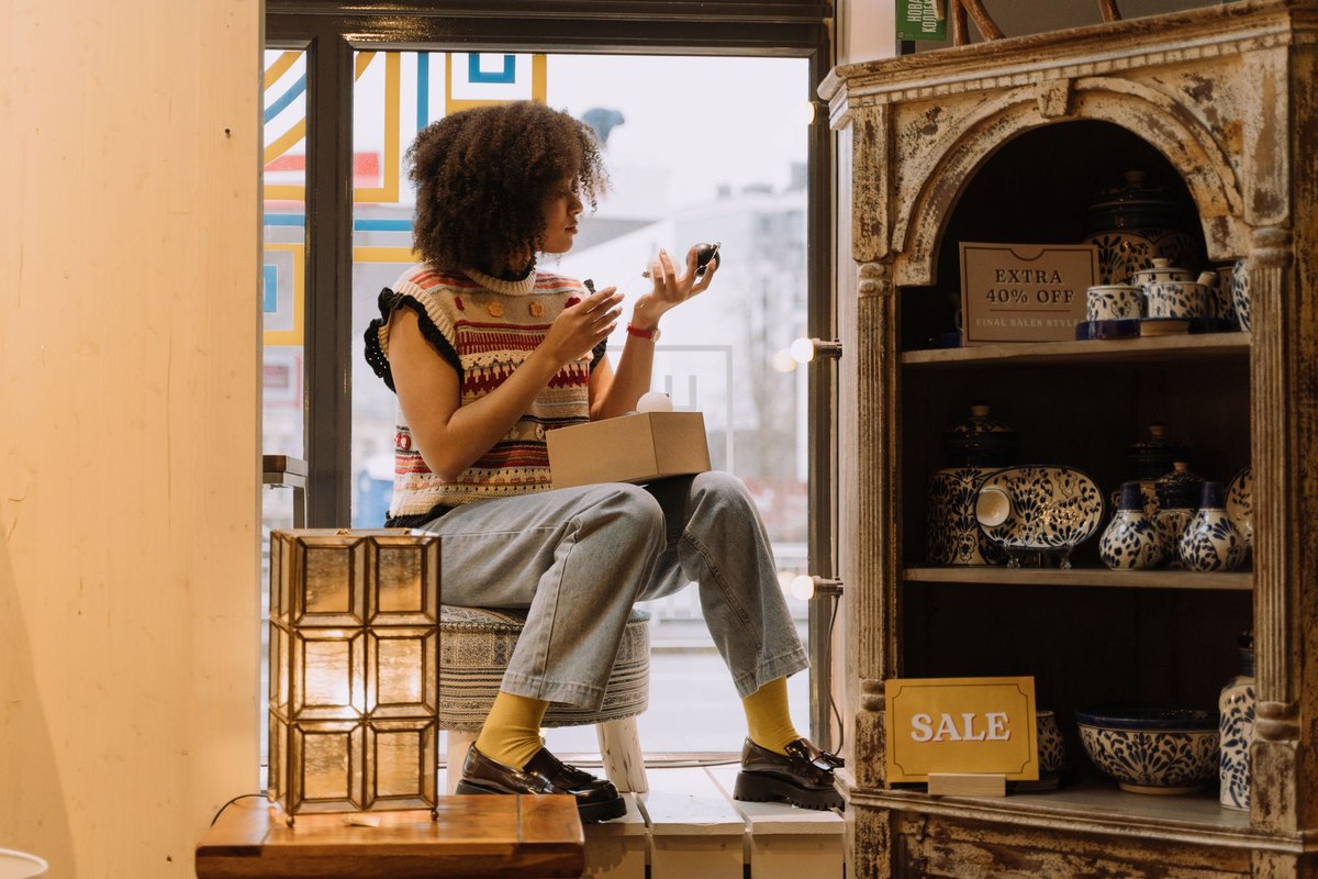 Kobieta w małym sklepie z ceramiką przy witrynie, obok półka z tabliczkami promocji SALE i EXTRA 40% OFF