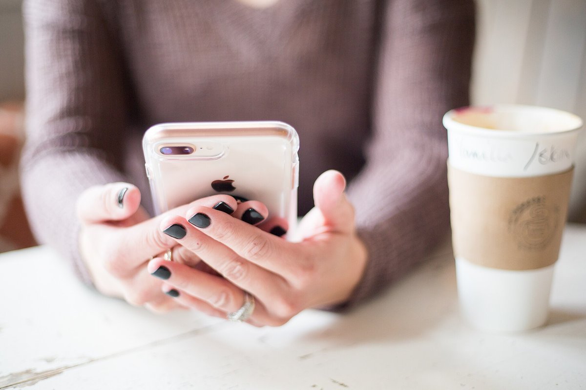 Przeglądanie produktów w reklamach Meta od 28 października: włączy się samo Kobieta trzyma w dłoniach telefon, obok stoi kubek z kawą na wynos