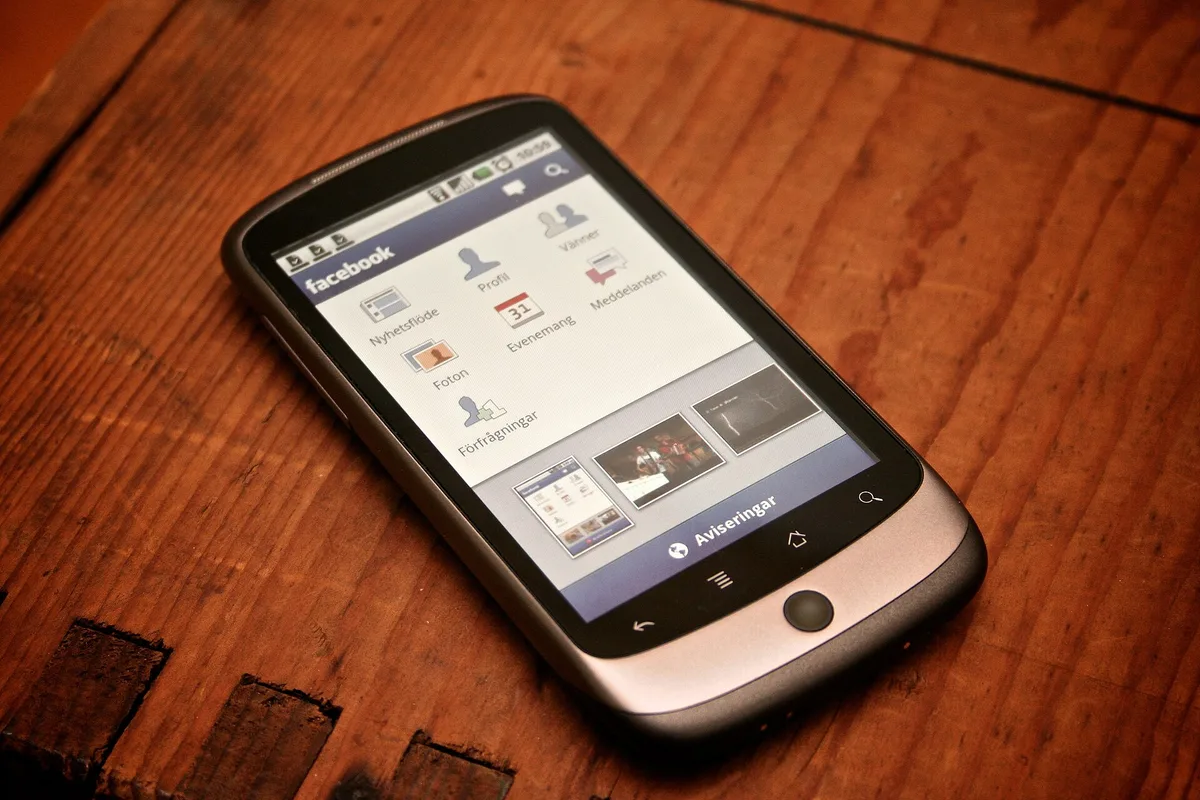 Nowe zasady reklam Meta od 30 października: co sprawdzić w małej firmie Smartfon z otwartą aplikacją Facebook z menu skrótów, leżący na drewnianym blacie