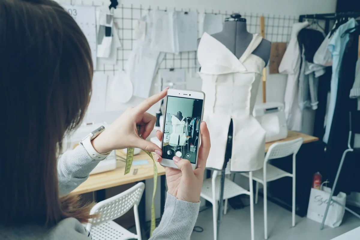 Projektantka robi smartfonem zdjęcie niedokończonego ubrania na manekinie w swojej pracowni krawieckiej